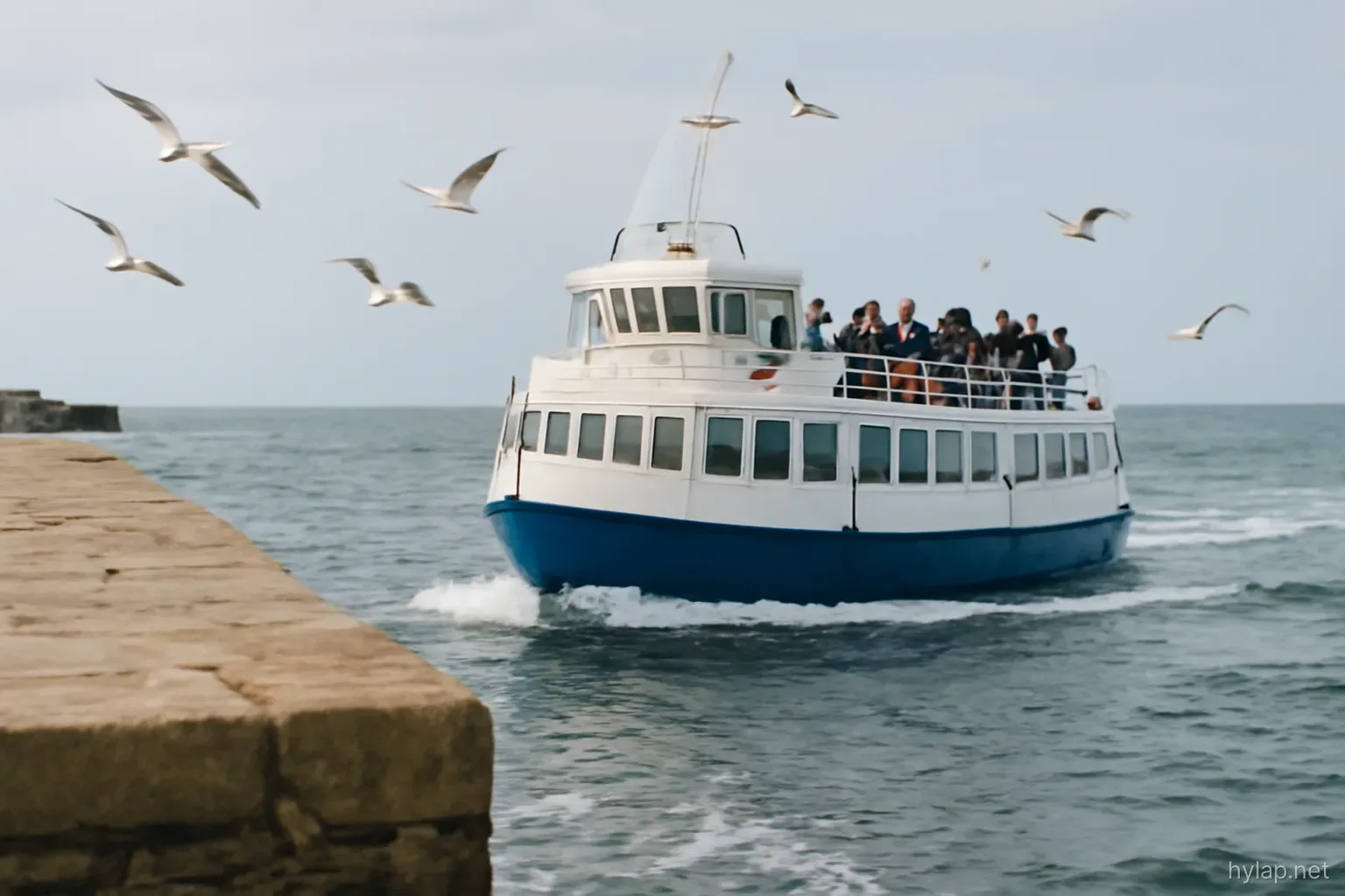 a ferry pulling away from a stone quay with gulls following and passengers at the rail