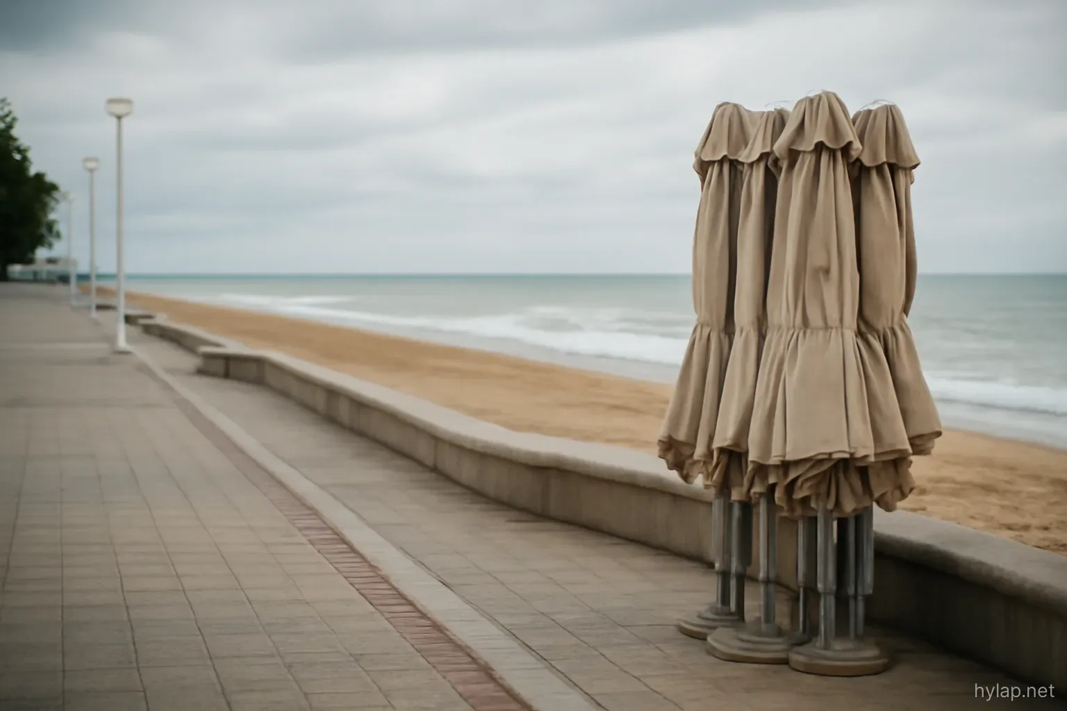 a beachfront promenade with folded umbrellas stacked and no people, overcast sky above