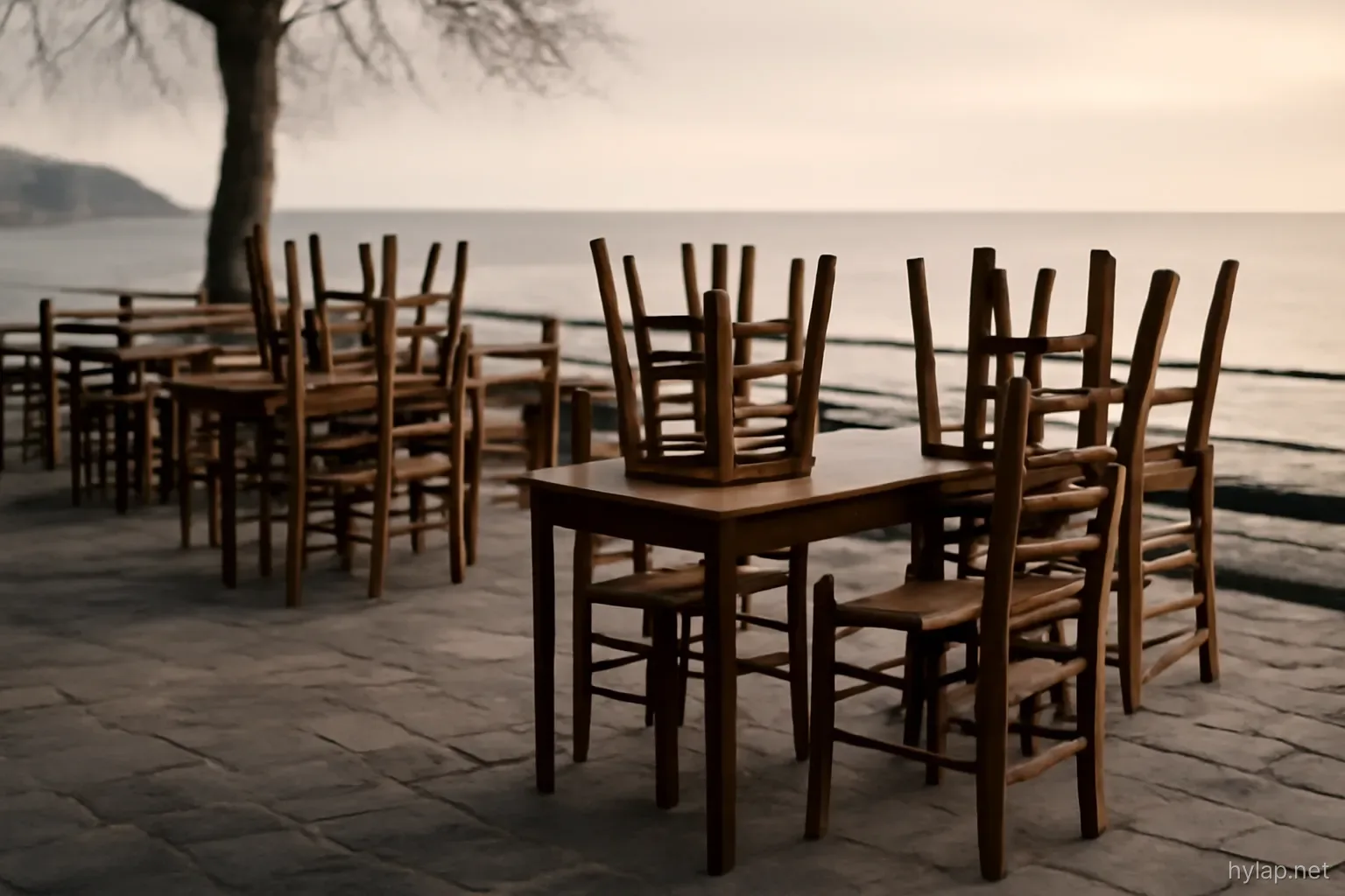 an empty taverna terrace with chairs stacked on tables facing the water in low winter light